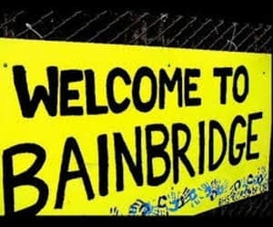 A yellow sign with black text reads "WELCOME TO BAINBRIDGE." Blue handprint decorations are visible along the bottom edge of the sign.