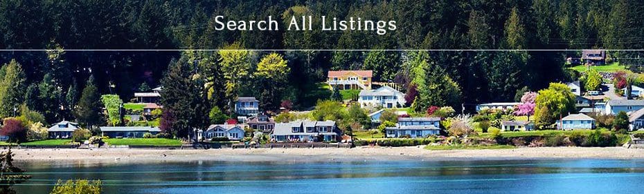 Panoramic view of a waterfront community with houses surrounded by trees, a beach, and a body of water in front. Text at the top reads "Search All Listings.