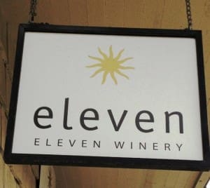 A hanging sign for Eleven Winery features a yellow starburst logo above the text "eleven" and "ELEVEN WINERY" in black letters.