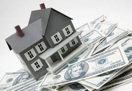 A model house sits on a scattered pile of U.S. dollar bills.