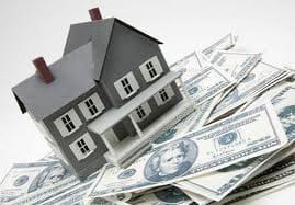 A model house is placed on top of a scattered pile of US dollar bills.