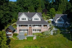 Aerial view of a large two-story house with a garden, surrounded by trees, and another smaller building nearby.