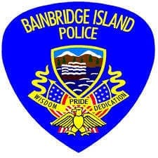 Logo of the Bainbridge Island Police featuring an eagle, U.S. flags, and a shield with mountains and water. Text reads: "Bainbridge Island Police" and "Wisdom, Pride, Dedication.