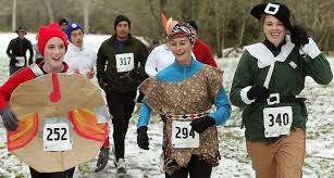 A group of runners, some in costumes including a pie, a caveman, and an elf, participate in a snowy race, each wearing numbered bibs.