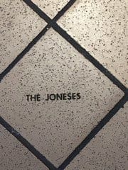 Close-up of a tiled wall with the words "THE JONESES" written in black on one of the tiles.