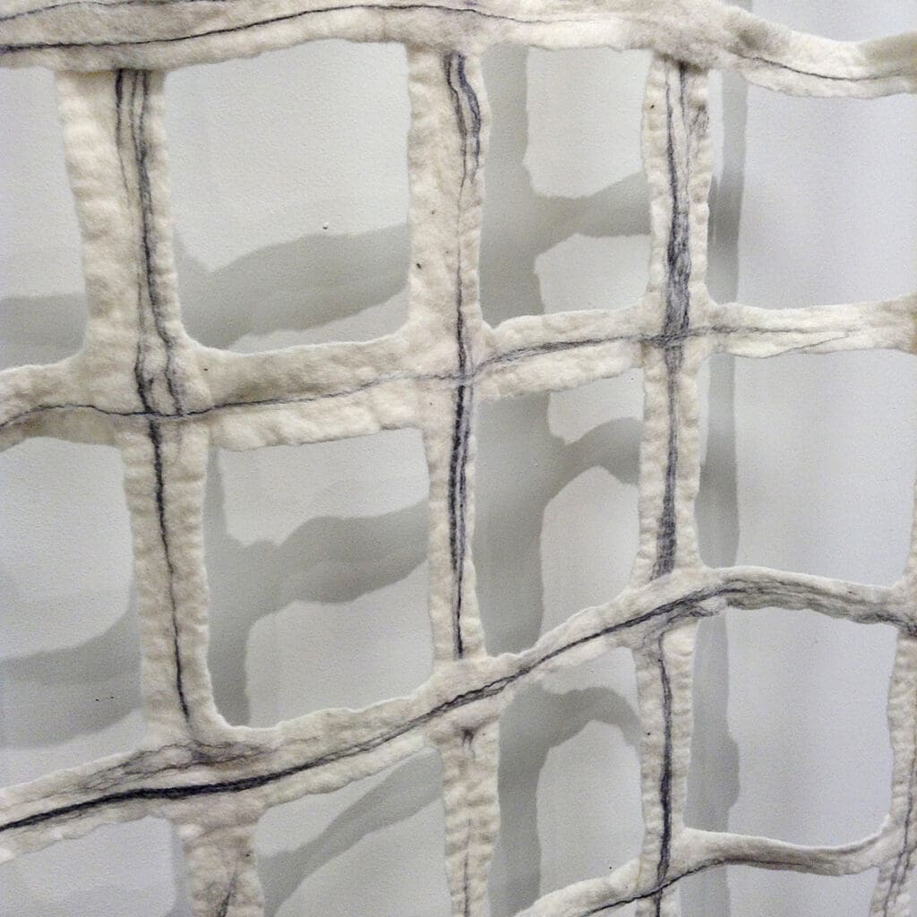 A close-up of a white fabric with a grid-like pattern, featuring irregular, hand-stitched lines that create a textured surface.