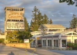 Image of a Town and Country shopping center with a large sign and multiple storefronts, trees in the background, and a clear sky visible.