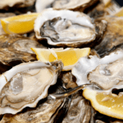 Opened oysters on the half shell are served on a platter with lemon wedges.