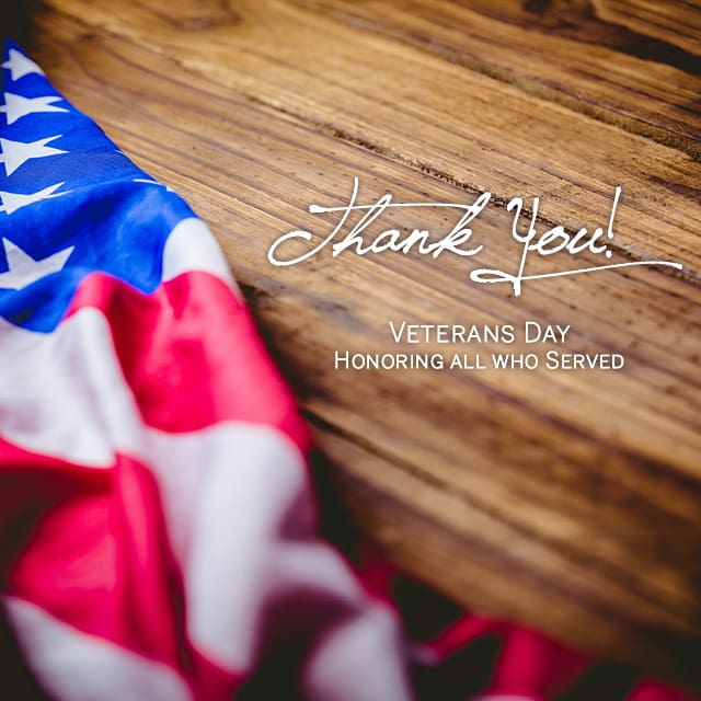 An American flag is draped over a wooden surface with the text: "Thank You! Veterans Day - Honoring all who Served.