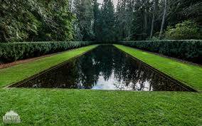 A rectangular reflective pool is surrounded by neatly trimmed grass and hedges, with trees in the background.