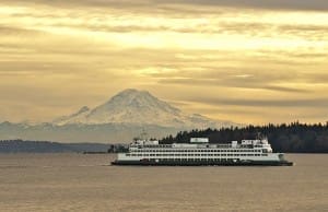 A ferry travels across a body of water with a mountainous landscape and a partly cloudy sky in the background.