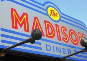 Sign for "The Madison Diner" with bold red and yellow lettering on a gray and blue background.