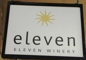 A hanging sign for Eleven Winery features a yellow starburst logo above the text "eleven" and "ELEVEN WINERY" in black letters.