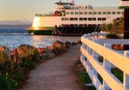 A ferry docked at a pier during sunset with a gravel path and white fence in the foreground.