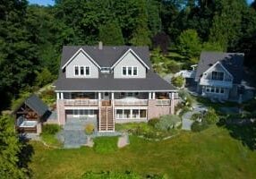 Aerial view of a large two-story house with a garden, surrounded by trees, and another smaller building nearby.