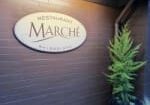 Sign for Restaurant Marché on a brick wall next to a potted plant.