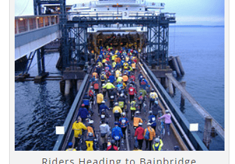 A large group of cyclists in colorful attire boarding a ferry at a dock. The caption reads, "Riders Heading to Bainbridge.