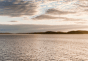 A calm body of water with a distant landmass under a partly cloudy sky during sunset.