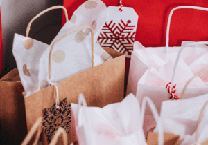 A collection of gift bags made of brown, red, and white paper, filled with tissue paper. Some bags feature snowflake designs and tags.