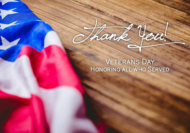 An American flag is draped over a wooden surface with the text: "Thank You! Veterans Day - Honoring all who Served.