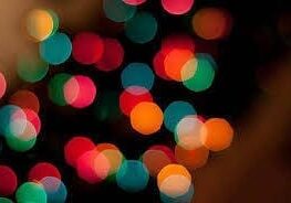 Blurred colorful lights on a dark background, creating a bokeh effect with red, green, orange, and blue hues.