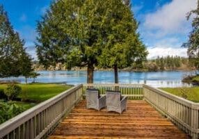 Two chairs on a deck overlooking a lake.