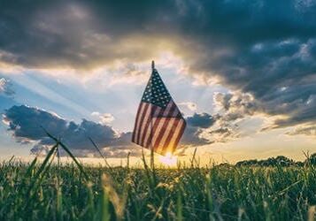 American flag waving in a field at sunset.